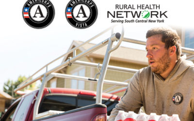 A man wearing a gray AmeriCorps NCCC sweatshirt unloading water out of a truck with the AmeriCorps, AmeriCorps Vista and Rural Health Network logos above him